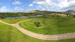 A golf course with a stone pathway, water bodies, and distant wind turbines. - VILAS ESPÍRITO SANTO by brugrani (Porto Santo)