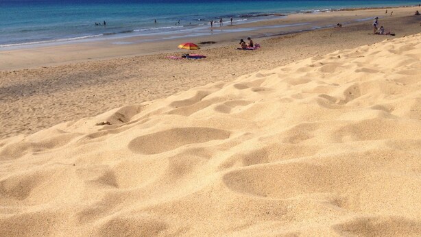 A sandy beach with footprints leading to the water, a few people, and a colorful umbrella. - VILAS ESPÍRITO SANTO by brugrani (Porto Santo)