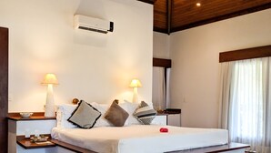 Une chambre d’hôtel avec un plafond en bois, un lit avec une literie blanche, deux lampes de chevet, une table de chevet, une fenêtre avec des rideaux et un plancher en bois.