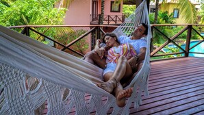 Un couple se détend dans un hamac sur une terrasse en bois, avec une piscine en arrière-plan.