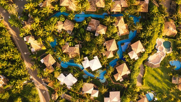 Vue aérienne d’un complexe hôtelier comprenant plusieurs hébergements de type bungalow, une fontaine centrale et une végétation tropicale luxuriante.