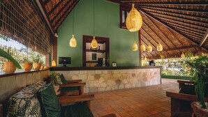 Un espace d’accueil avec un mur en pierre, des bancs en bois et des lampes en osier suspendues.
