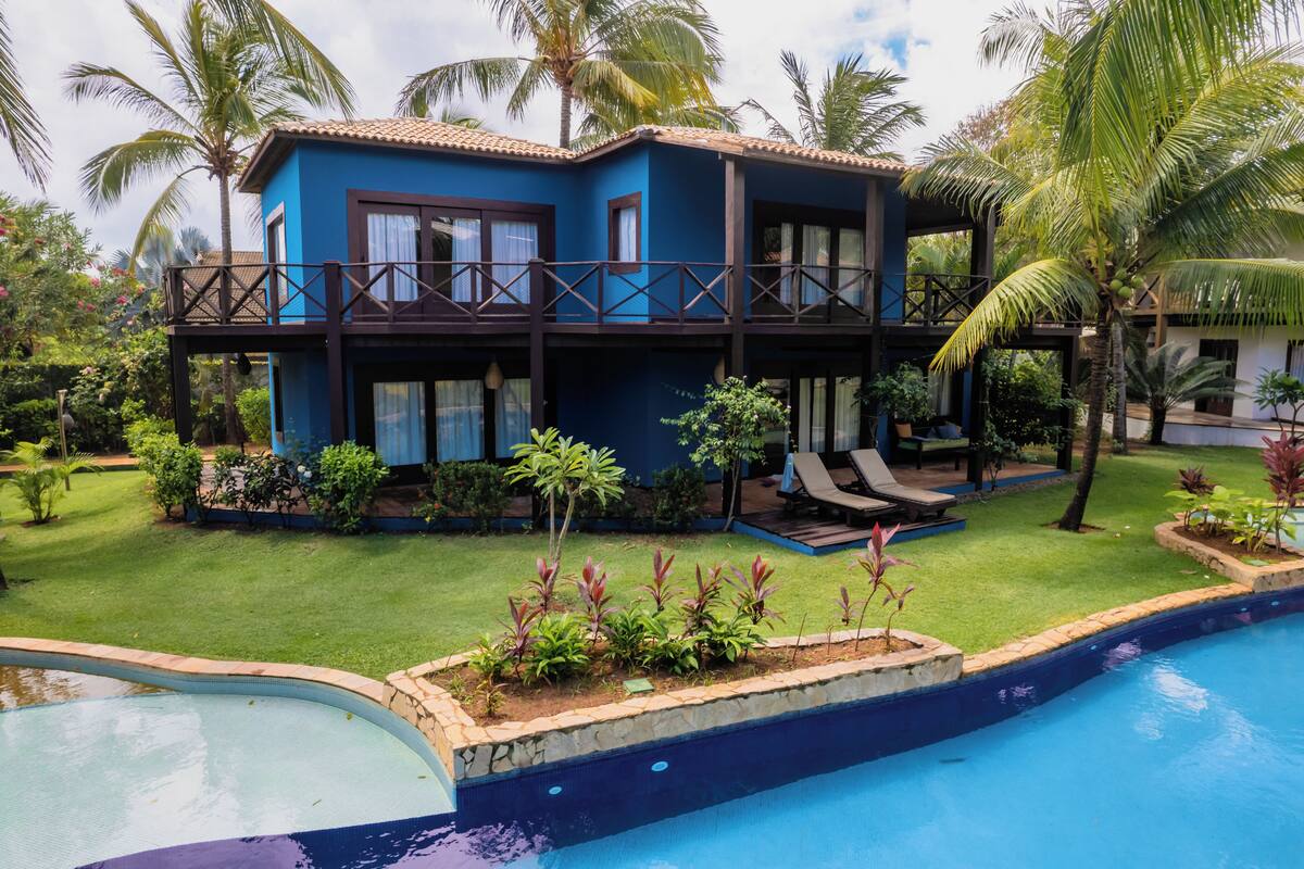 Un bâtiment à deux étages doté d’un balcon, d’une piscine et d’un aménagement paysager de style tropical.