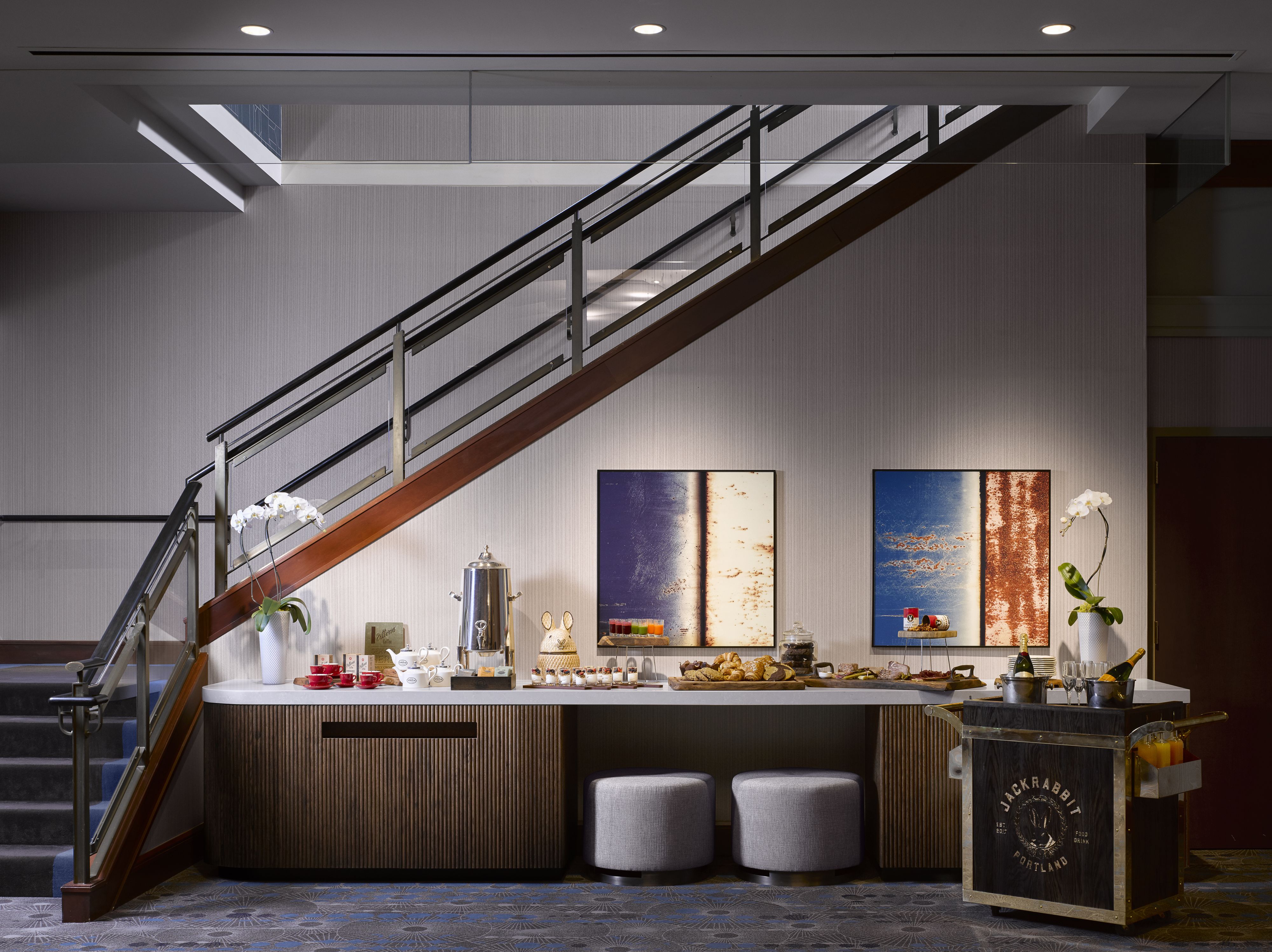 Eine moderne Hotelhalle mit einer Treppe, einer Bar mit einem Jackrabbit Schild und zwei großen abstrakten Bildern an der Wand.