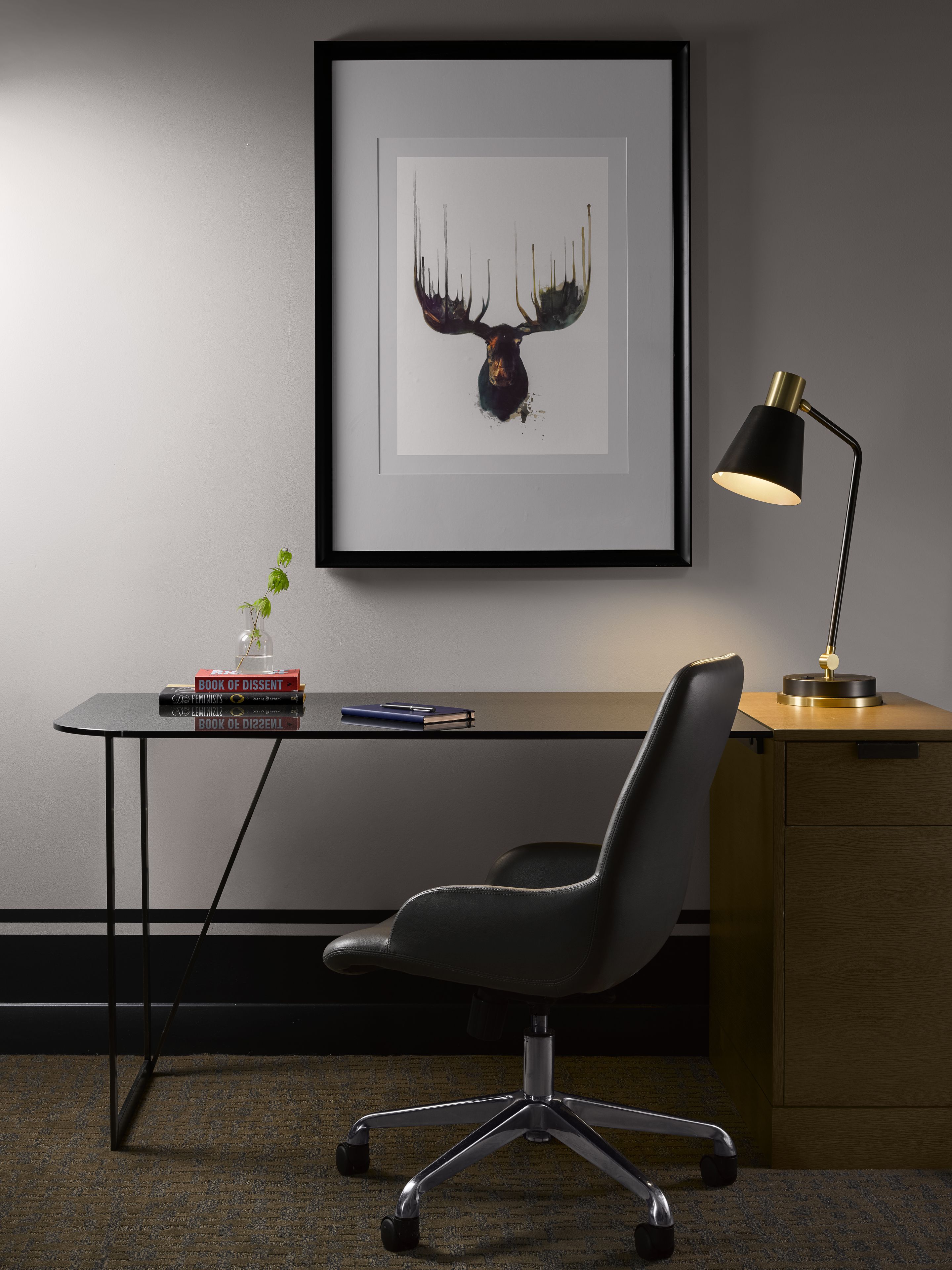 A modern office desk with a framed artwork, a lamp, and books.
