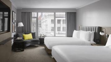 Une chambre d’hôtel avec deux lits, un canapé, un bureau et une grande fenêtre donnant sur des immeubles.