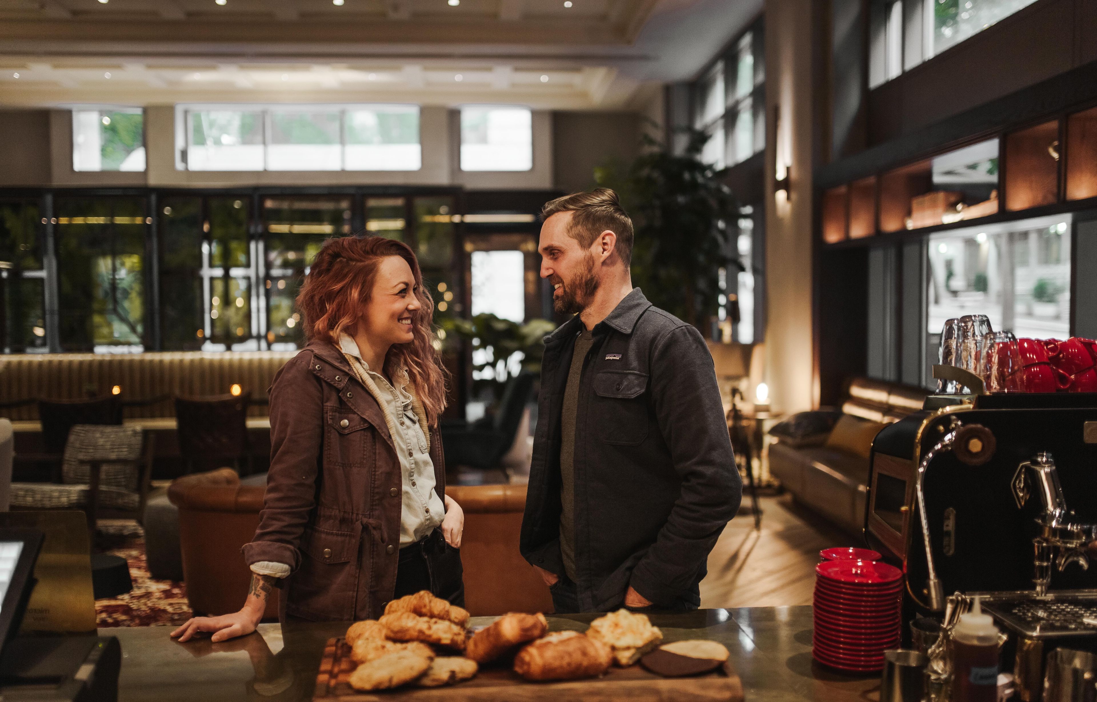 Una pareja parada en un interior moderno con una zona de bar al fondo.