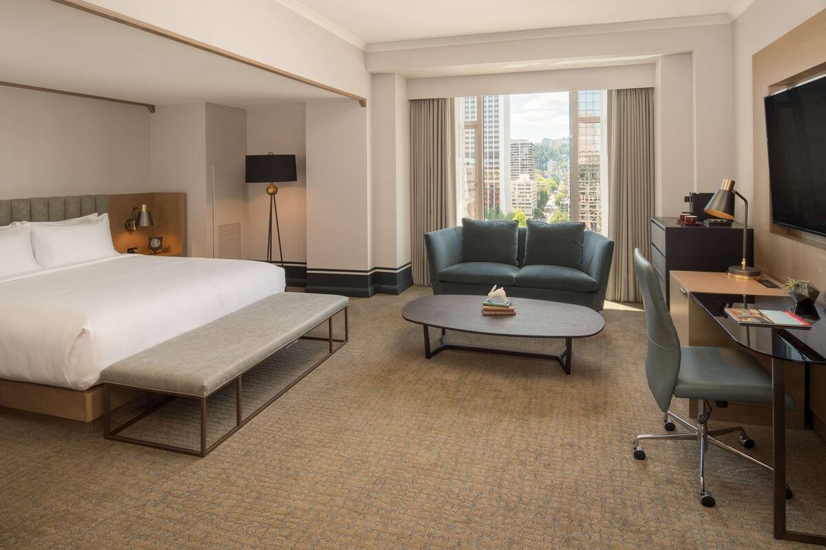 A hotel room with a bed, a desk, a chair, a sofa, and a coffee table.