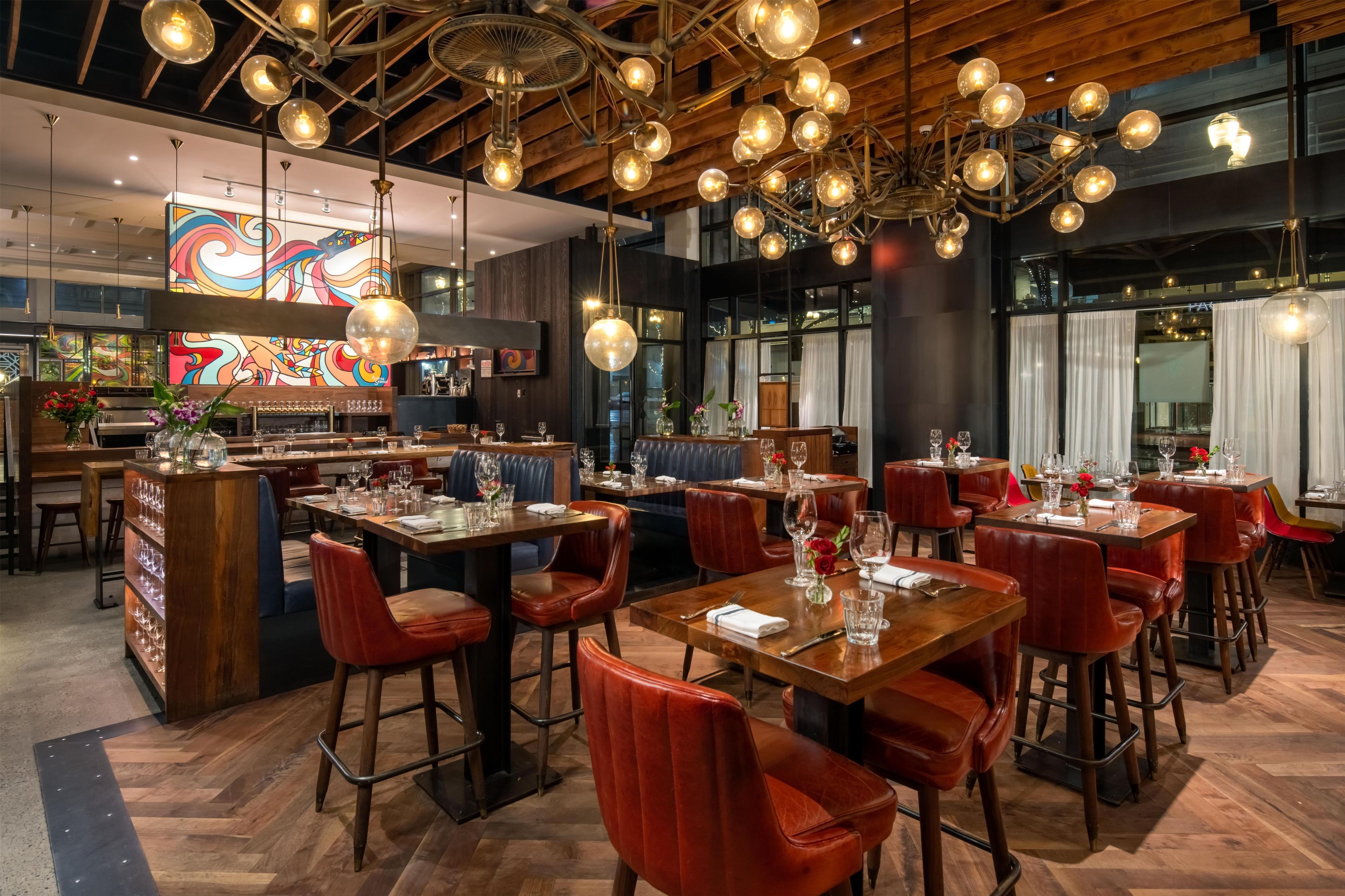 A restaurant interior with wooden tables, red leather chairs, and a bar area.