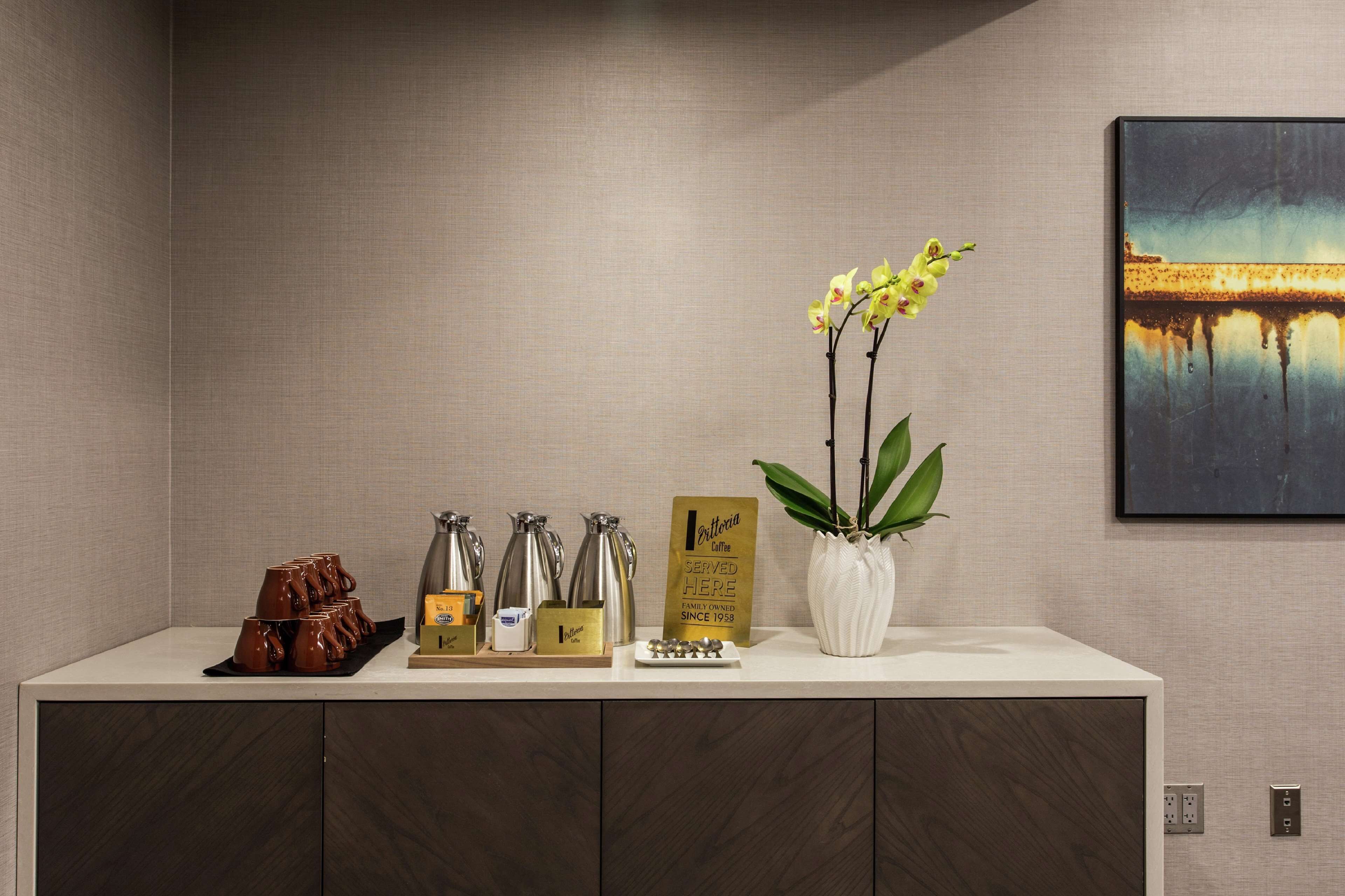 A reception area with a coffee station, a sign indicating the coffee is family-owned since 1938, and a vase with orchids.