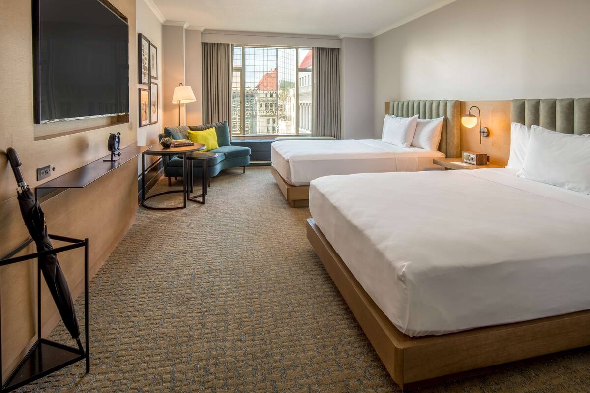 A hotel room with two beds, a desk, a chair, a TV, and a window with a city view.
