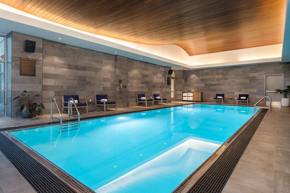 An indoor swimming pool with clear blue water, surrounded by lounge chairs and a wooden ceiling.