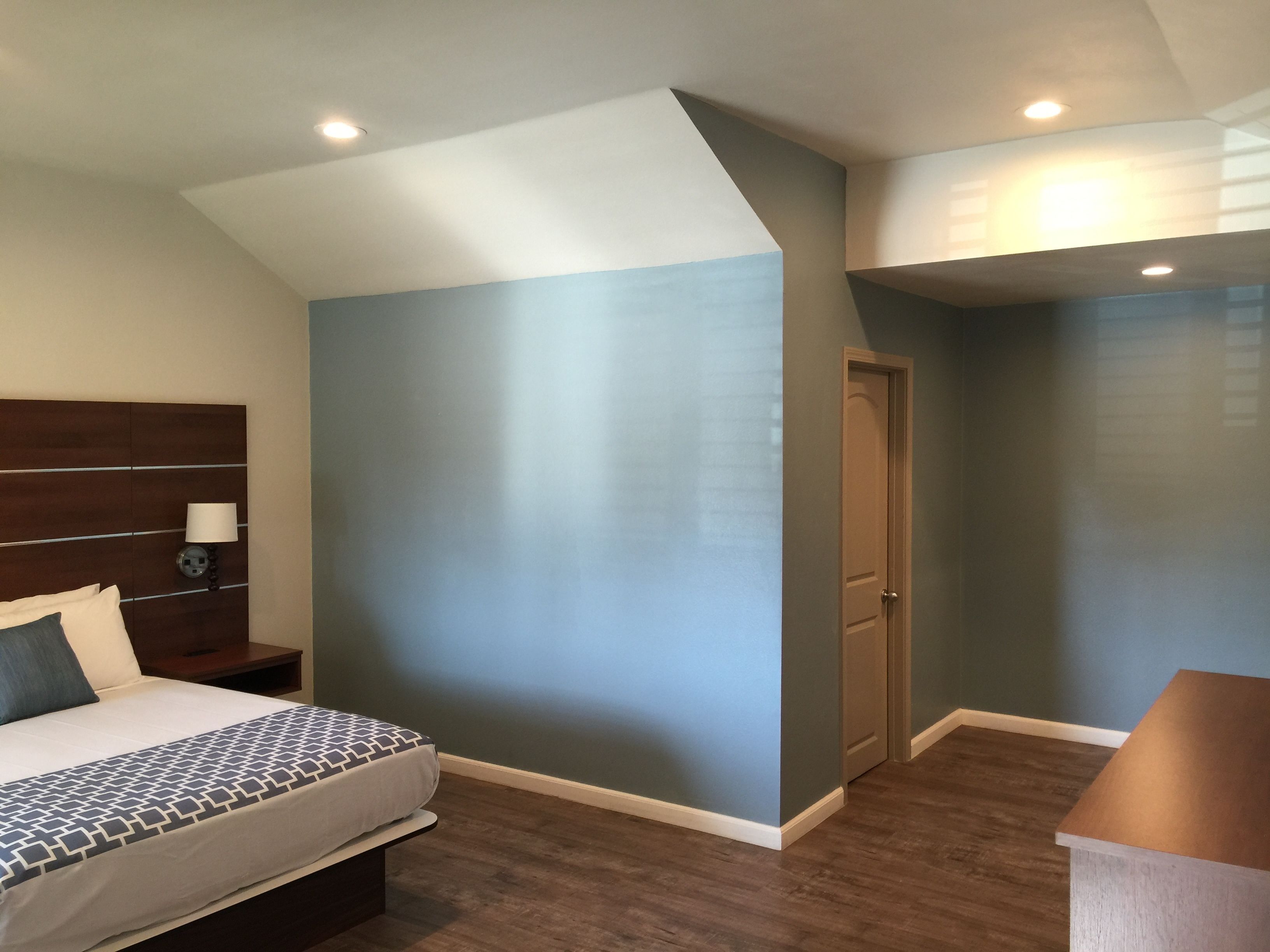 A bedroom with a bed, nightstands, a dresser, a door, and a ceiling with recessed lighting.