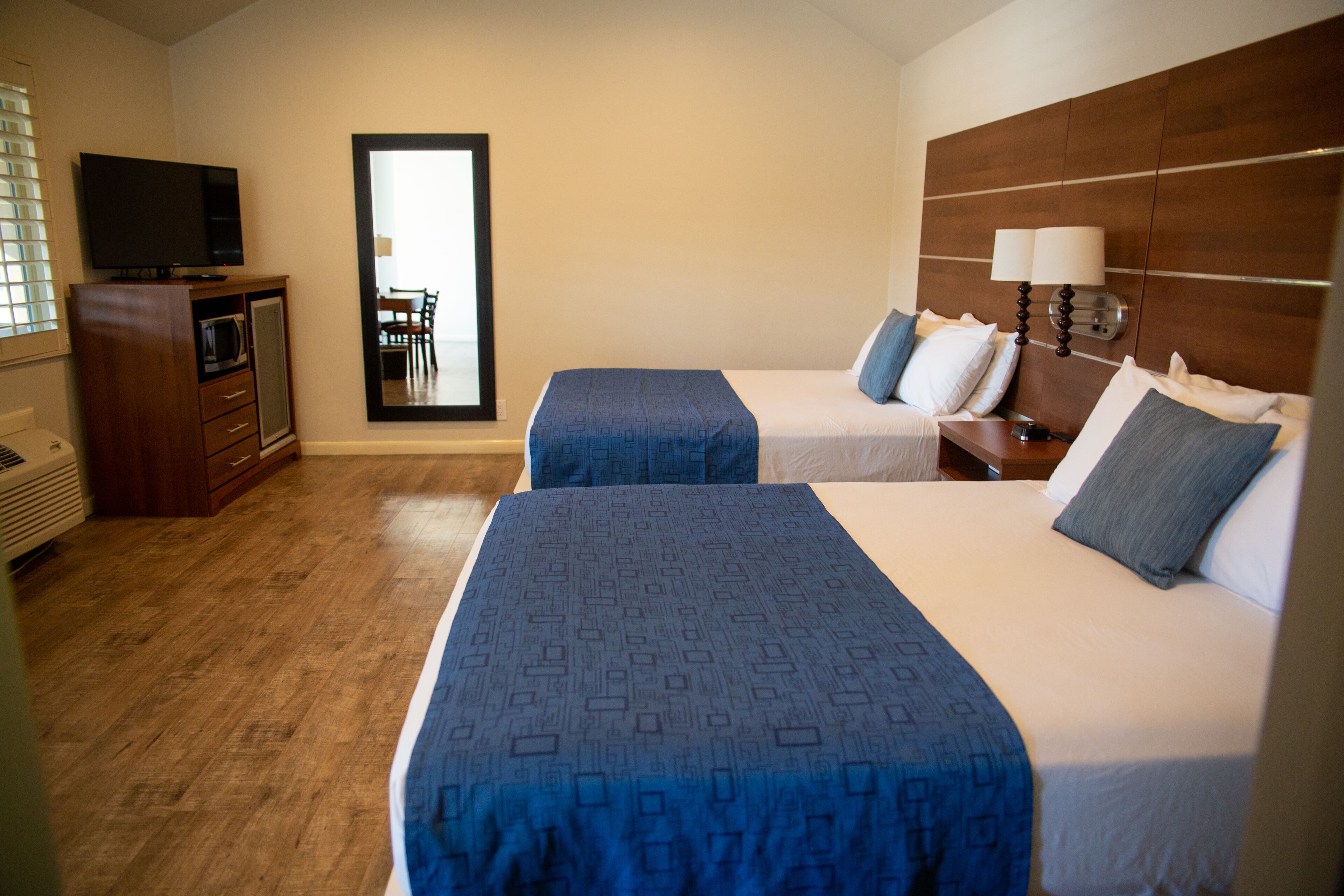 Quarto de hotel com duas camas, televisão, escrivaninha e espelho.