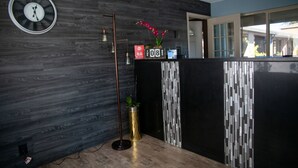 A reception area with a wooden wall, a black reception desk, a clock, and a tall floor lamp.