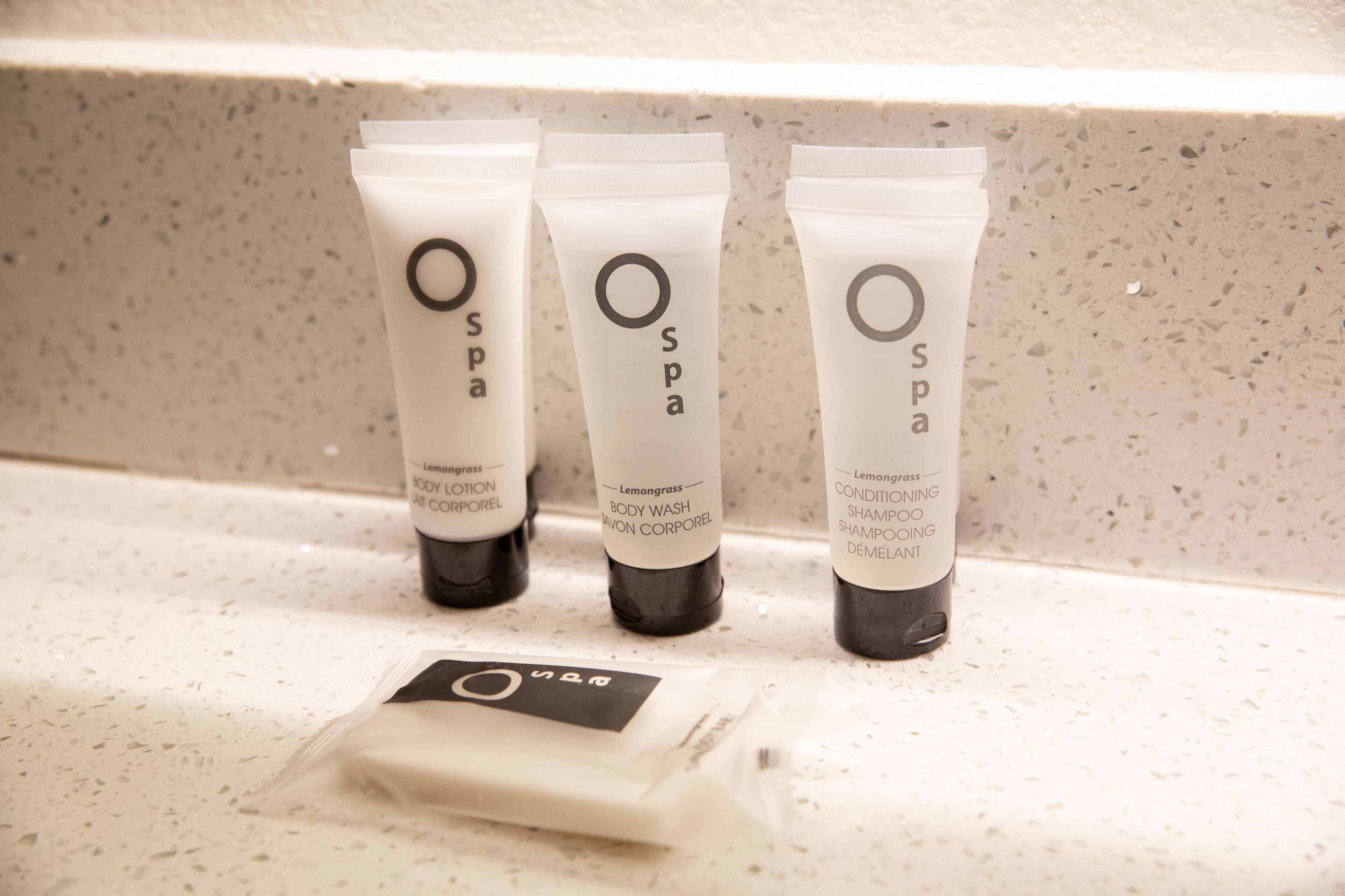 Three OSPA body wash tubes and a small sachet on a speckled countertop.