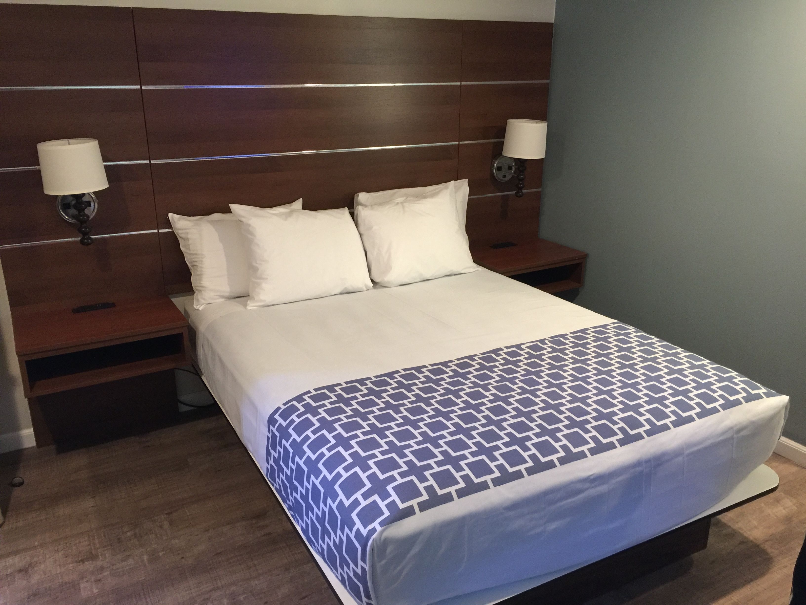 Una cama bien hecha con una colcha estampada, dos lámparas de noche y un cabecero de madera.
