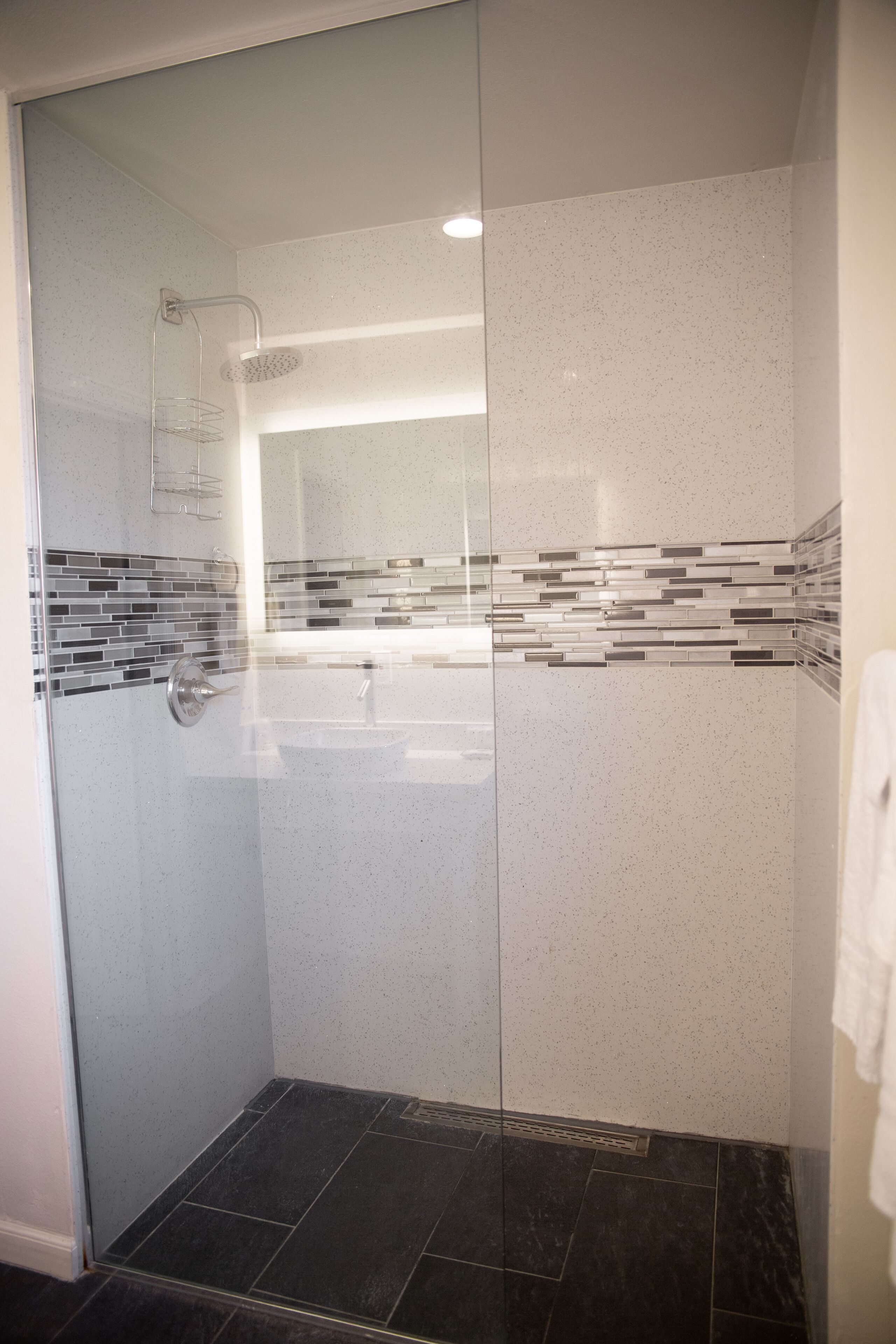 Eine moderne Dusche mit Glastür, Fliesenboden und Wand mit Mosaikfliesen.