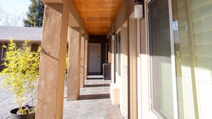 A covered outdoor corridor with wooden ceiling, concrete pillars, and large windows.