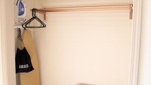 A closet with a hanging rack, an ironing board, and a bag labeled "HAIR DRYER".