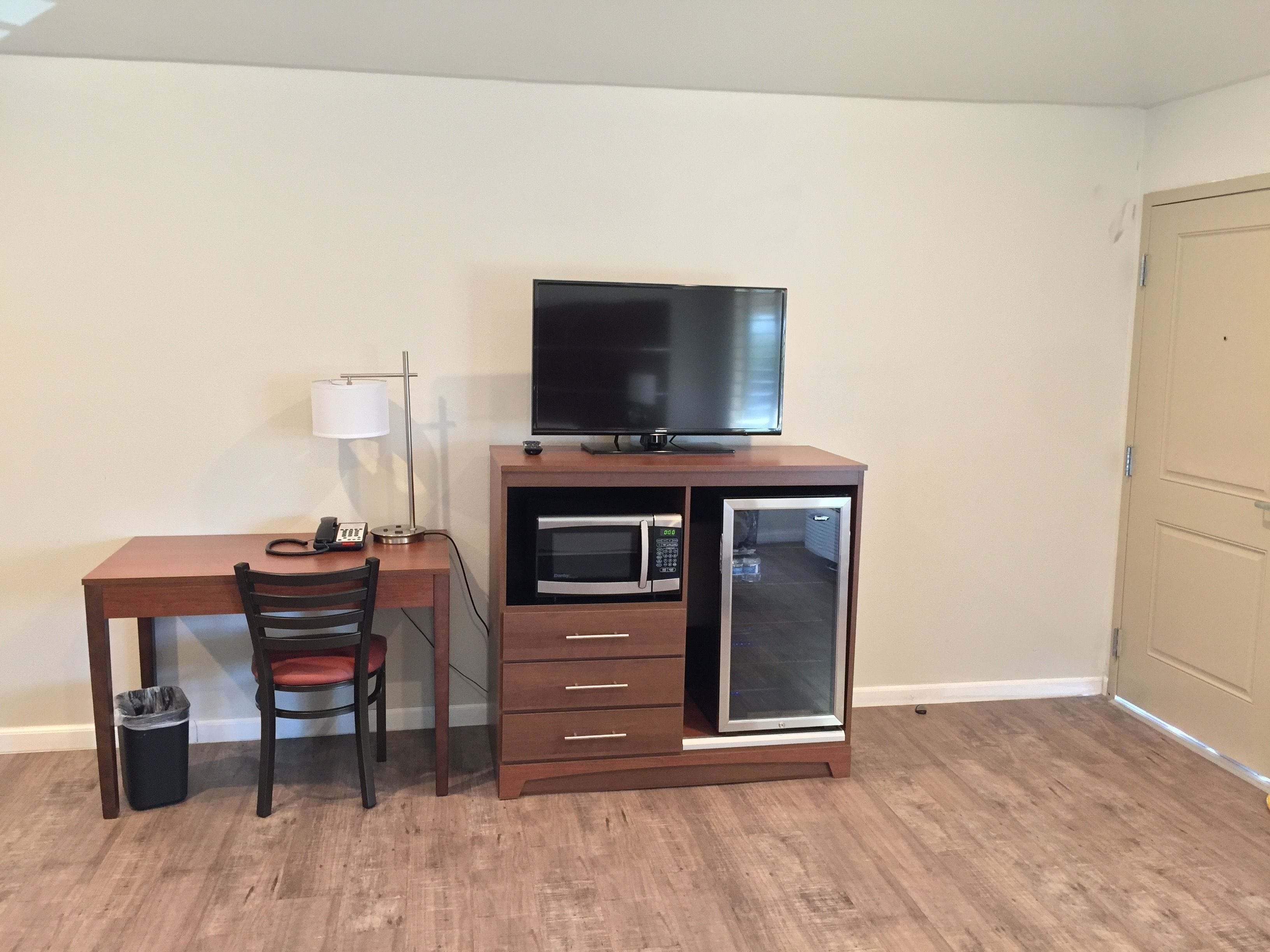 A compact room with a wooden desk, a chair, a television, a microwave, and a mini-fridge.