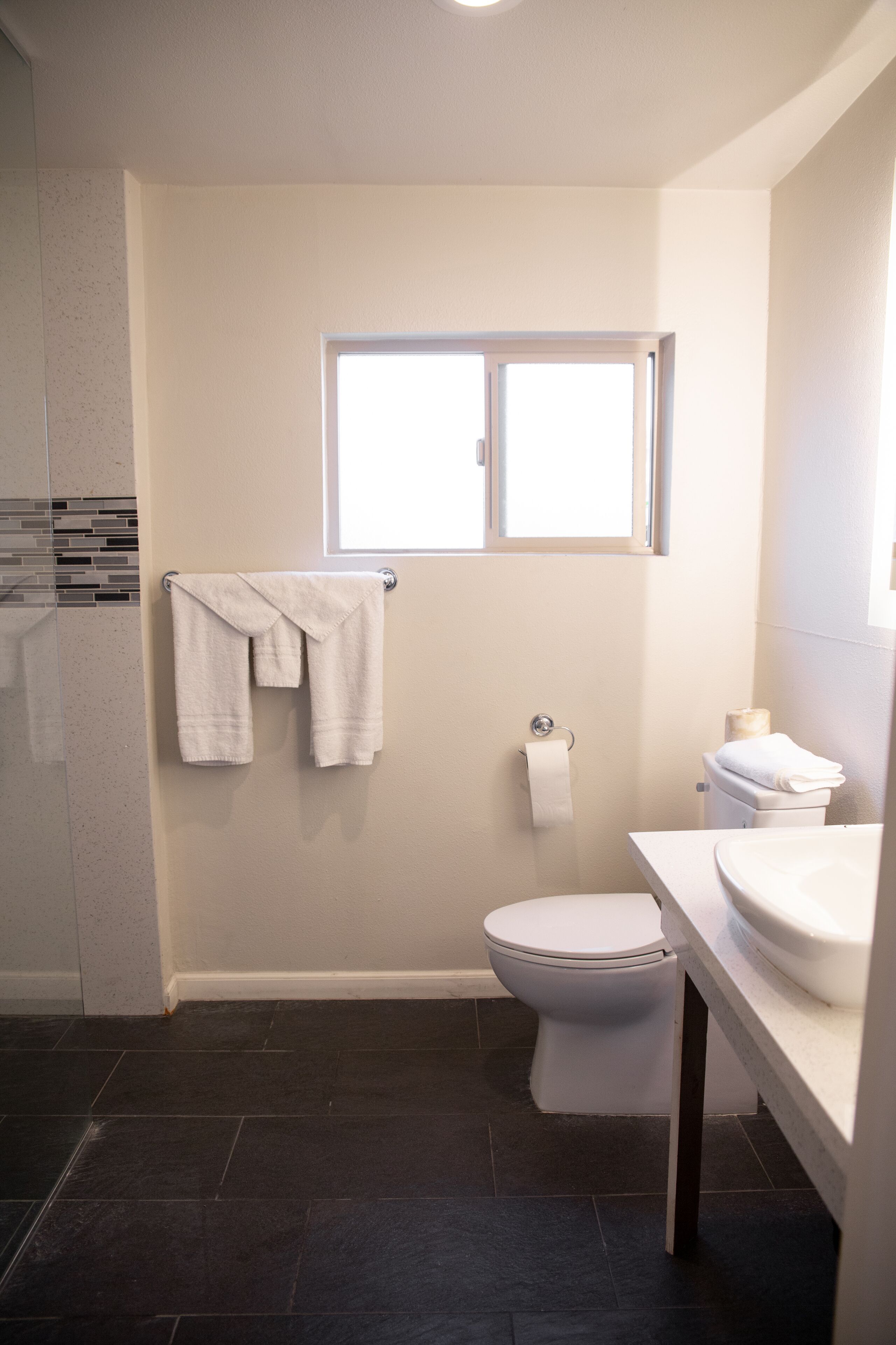 Ein Badezimmer mit Toilette, Waschbecken, Fenster und Handtuchhalter mit Handtüchern.