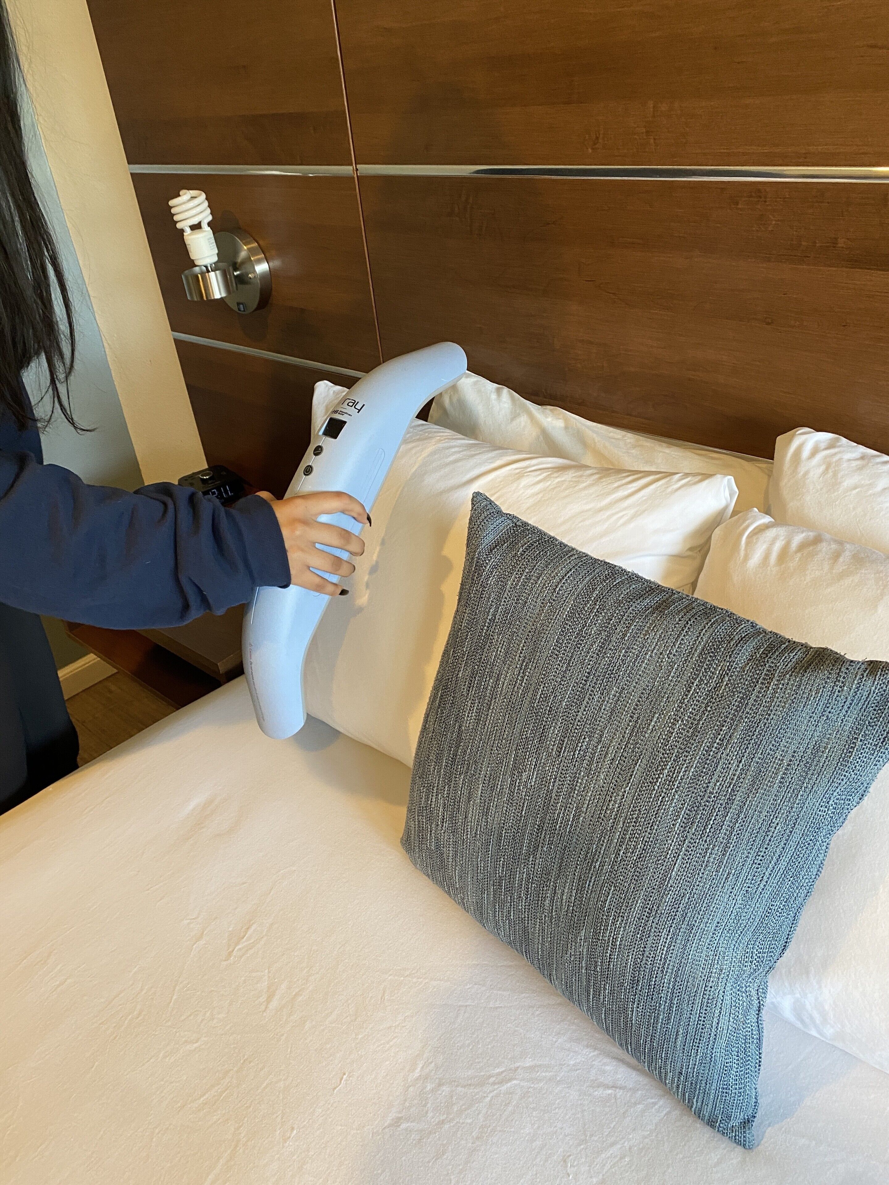A person using a massage device on a bed with white and gray pillows.