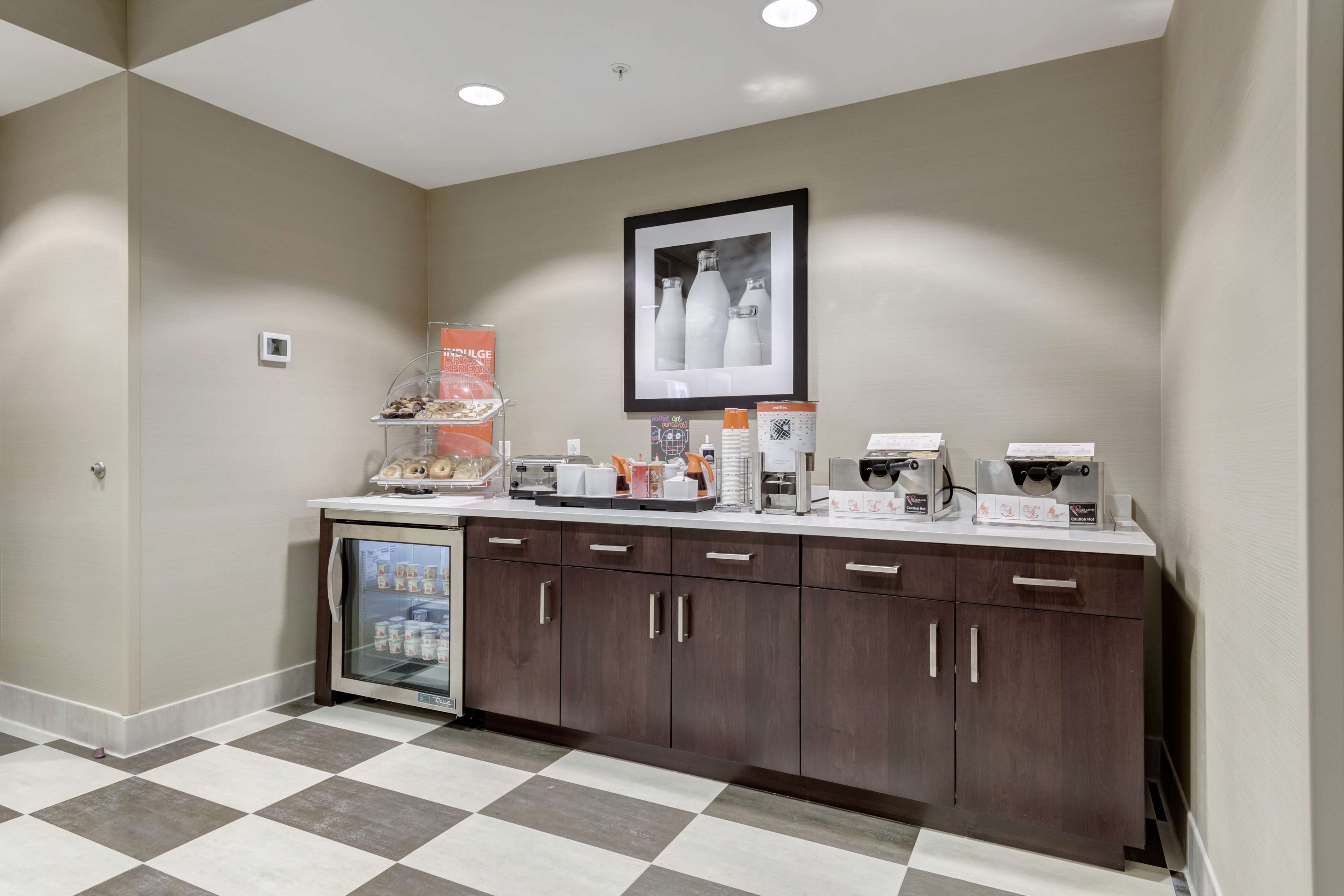 Una kitchenette con refrigerador, cafetera y diversos alimentos sobre la encimera.