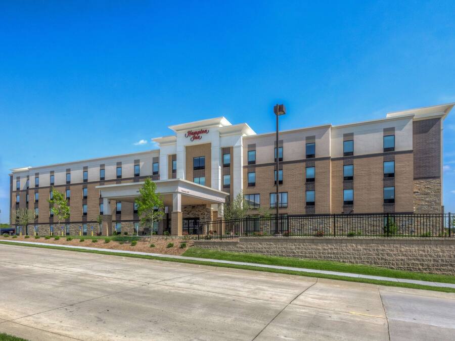 Un hotel Hampton Inn con un diseño moderno, que presenta fachada de ladrillo, múltiples ventanas y un área de entrada bien cuidada con un paseo techado.