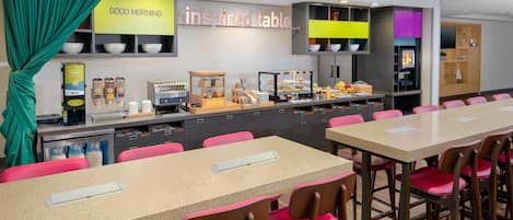 A breakfast area with a buffet setup, including a coffee machine, bowls, and a variety of food items.