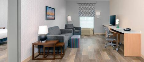 A hotel room with a sofa, a desk, a lamp, a chair, and a bedside table.