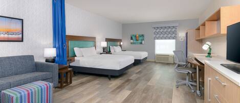 A hotel room with two beds, a desk, a chair, a sofa, and a colorful ottoman.