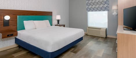 A hotel room with a bed, bedside table, lamp, TV, and a window with a view.