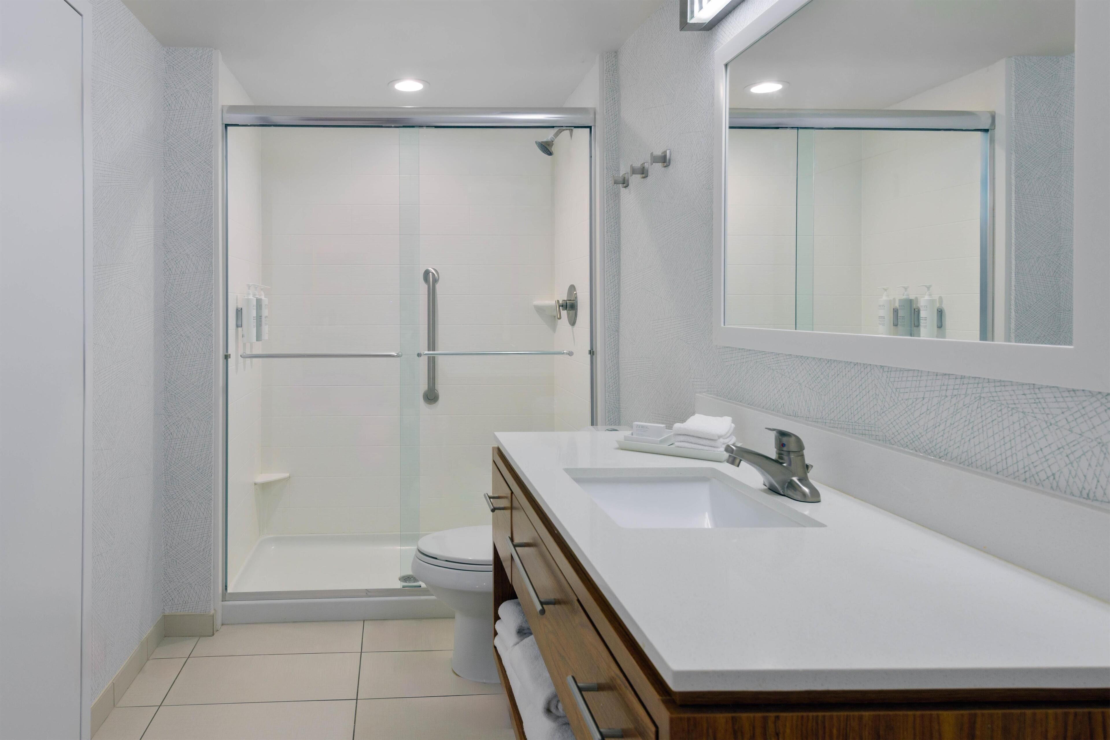 A modern bathroom with a glass-enclosed shower, a white sink, and a large mirror.
