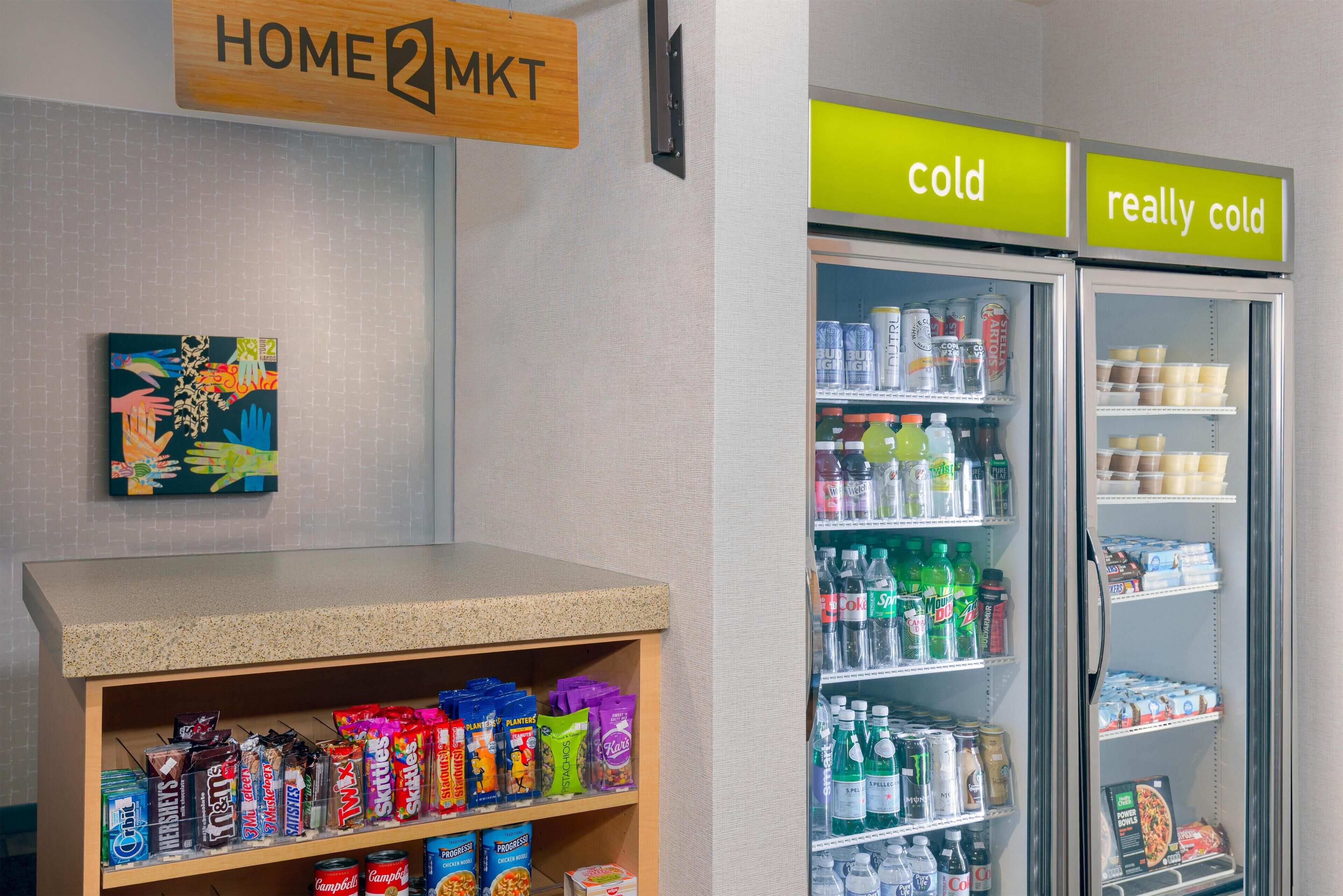Un espace de vente proposant des collations et des boissons, une enseigne indiquant « HOME 2 MKT », et deux réfrigérateurs étiquetés « froid » et « très froid ».