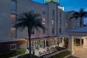 A hotel with a covered outdoor seating area, palm trees, and a sign reading "HOME 2". - Home2 Suites by Hilton Nokomis Sarasota Casey Key (Nokomis)