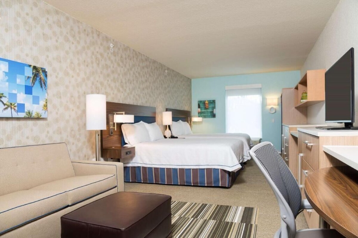 Habitación de hotel con cama, dos mesitas de noche, escritorio, silla, sofá y televisor.
