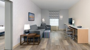 Ein Hotelzimmer mit einer Couch, einem Schreibtisch, einer Lampe, einem Fernseher und einem Fenster mit gemusterten Vorhängen.