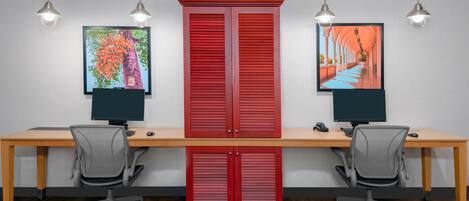 Un espace de travail comprenant deux bureaux, chacun équipé d’un écran d’ordinateur, de chaises de bureau et d’un meuble rouge.