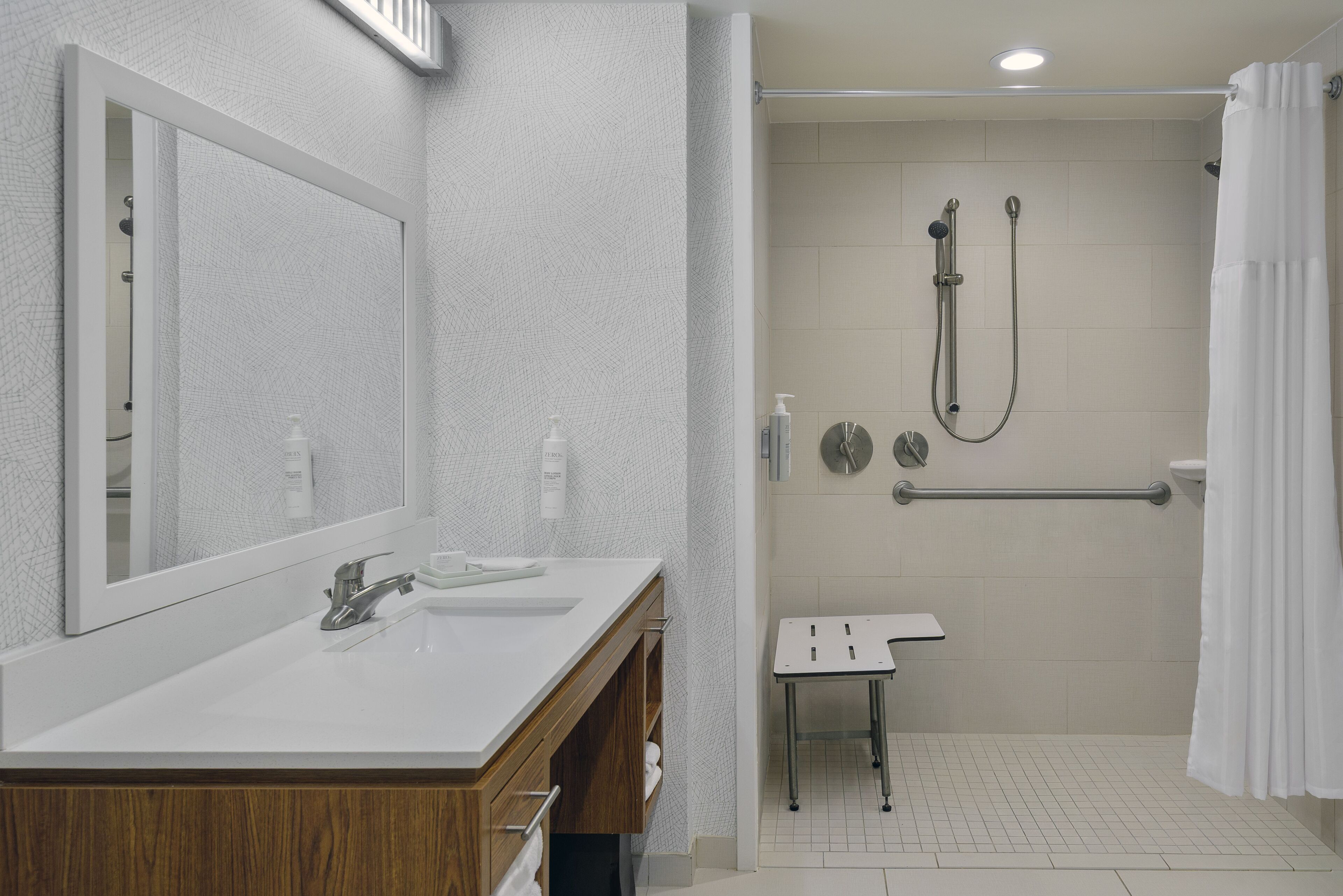 Un baño moderno con un espejo grande, lavamanos dobles, ducha con cabezal de ducha de mano y barra de apoyo.