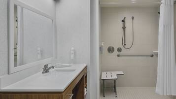 Un bagno moderno con un ampio specchio, due lavandini, una doccia con soffione manuale e una barra di sostegno.