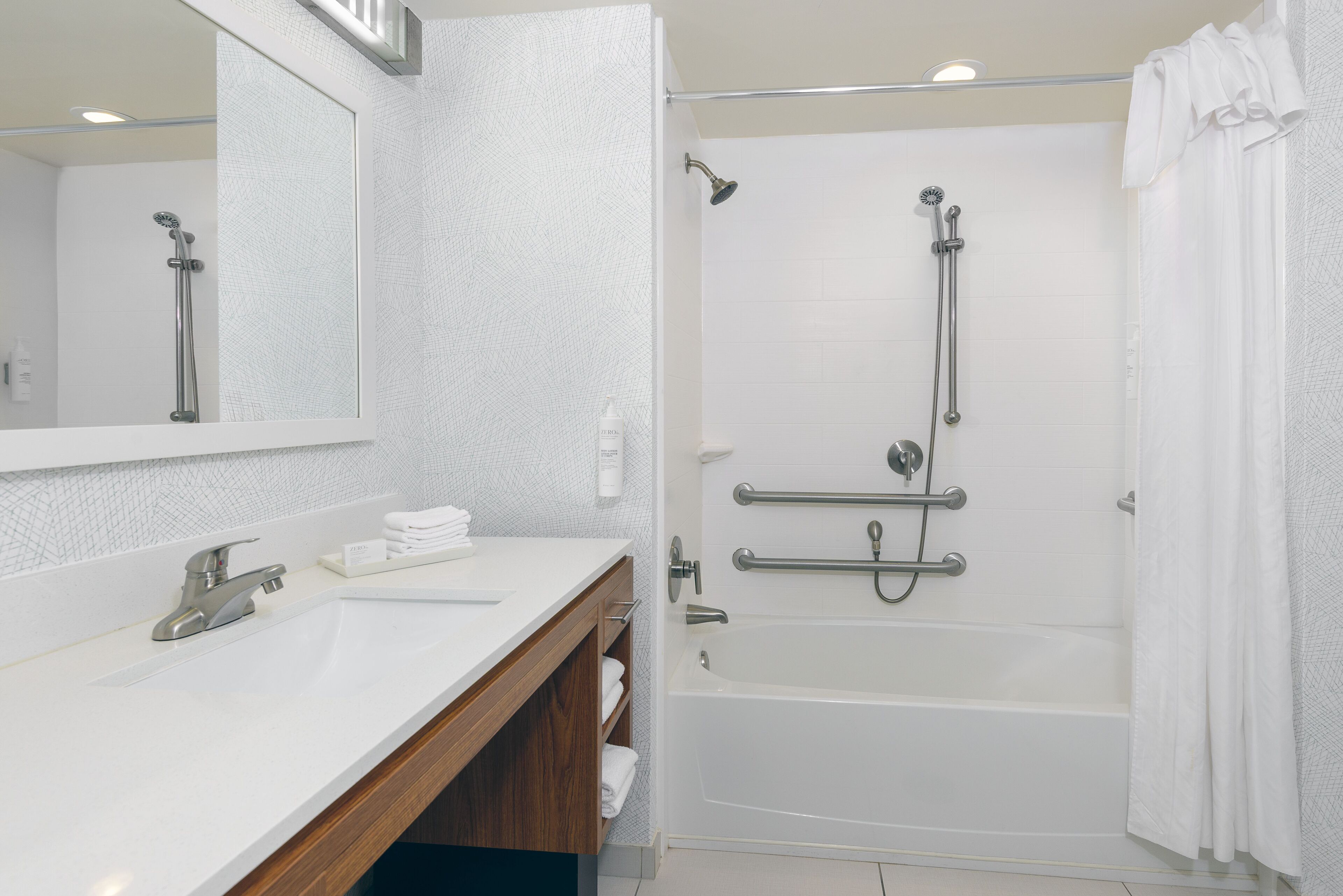 Une salle de bain moderne avec un lavabo blanc, un miroir, une douche équipée de barres d’appui et une baignoire.