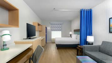 Una habitación de hotel con cama, escritorio con computadora, sofá y televisión.