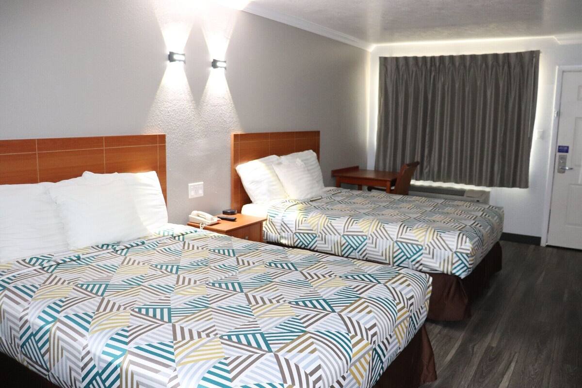 A hotel room with two beds, a desk, a chair, and a window with curtains.