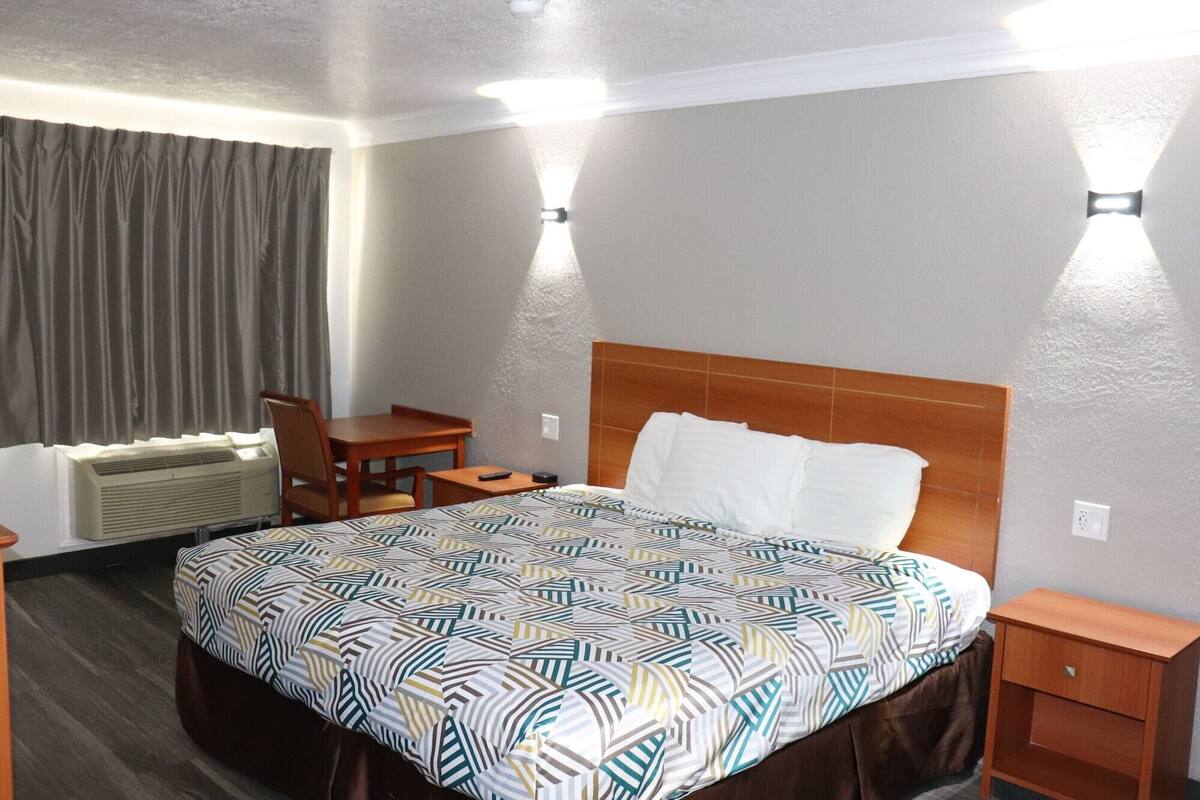A hotel room with a bed, a desk, a chair, and a small table.
