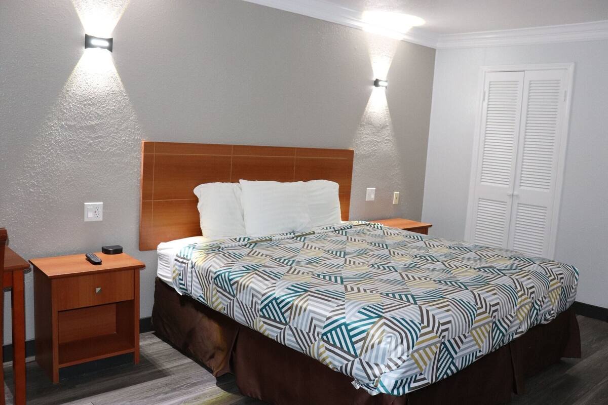 A hotel room with a bed, a nightstand, a bedside table, and a wardrobe.