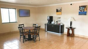 A dining area with a round table and four chairs, a coffee station with a coffee maker and cups, and a lamp on a side table. - Motel 6 Alvin, TX (Alvin)