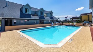 A swimming pool area with a blue building, a covered seating area, and a sign indicating an emergency phone. - Motel 6 Alvin, TX (Alvin)
