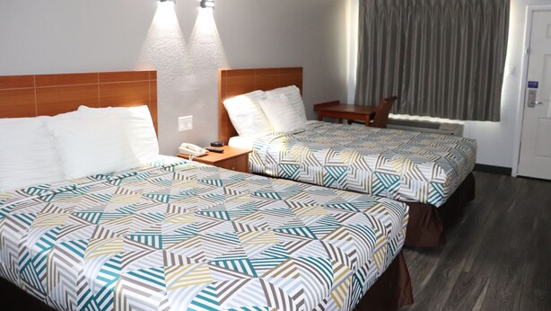 A hotel room with two beds, a nightstand, a chair, and a window with curtains. - Motel 6 Alvin, TX (Alvin)