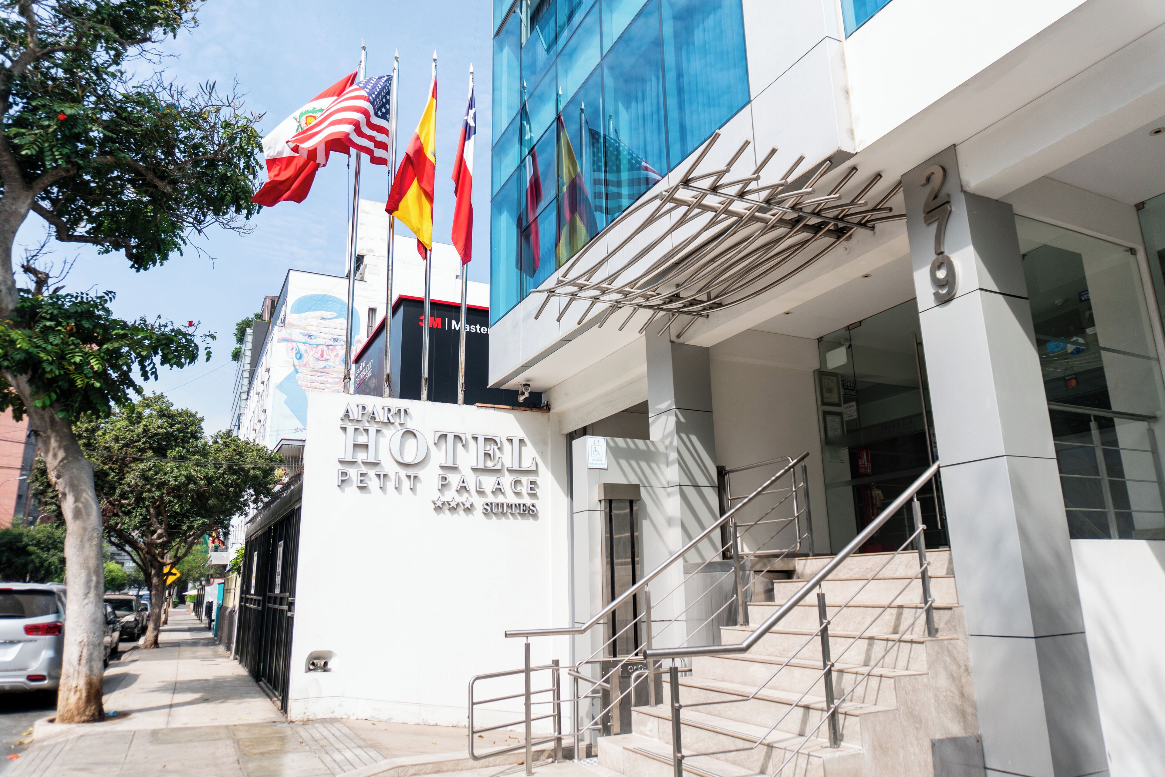 A hotel entrance with a staircase, flags, and a sign reading "APART HOTEL PALACE SUMMPS".